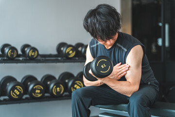 Young Asian man doing dumbbell training at fitness gym