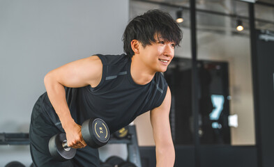 Plakat Young Asian man doing dumbbell training at fitness gym