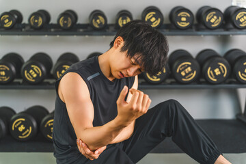 Young Asian man suffering from elbow pain while training at the gym