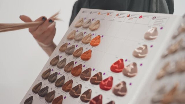 hair color swatch board held by person undetermined during salon consultation stylist points to warm red and brown shades while client examines glossy dye samples arranged in neat rows close framing