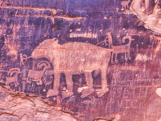 A rock with a drawing of a cow and a goat on it. The cow is surrounded by a group of goats