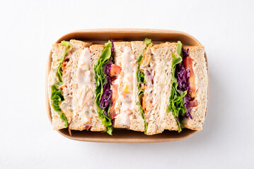 Sandwich tuna mayonnaise with whole wheat bread, lettuce, carrot, tomato and purple cabbage in biodegradable food box on white background