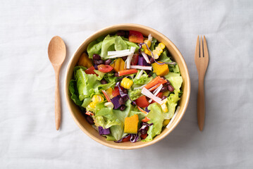 Healthy vegetable salad with lettuce, tomato, pumpkin, corn, purple sweet potato, cabbage, azuki bean and crab stick in takeout bowl with spoon and fork, Top view