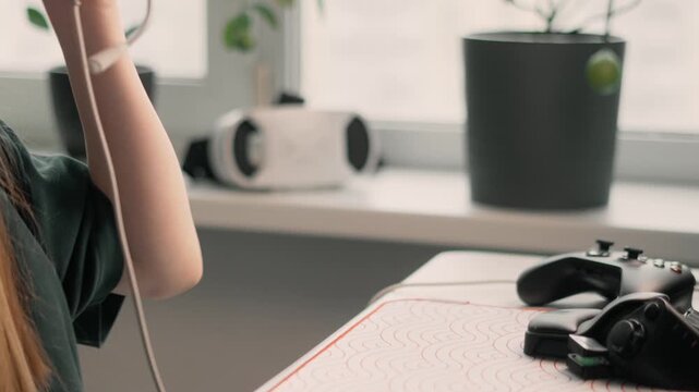 Cozy home gaming setup with young woman playing console game using controller and headphones. Comfortable interior, soft daylight, relaxed mood, personal space for rest, modern home entertainment