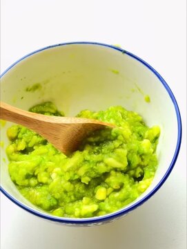 Stirring mashed avocado in the bowl with a spoon.