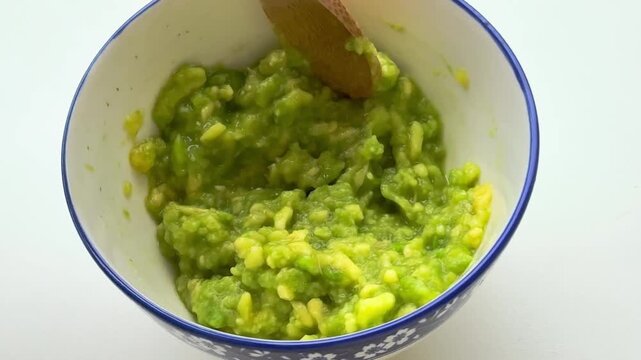Stirring mashed avocado in the bowl with a spoon.