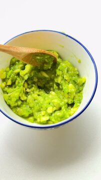 Stirring mashed avocado in the bowl with a spoon.