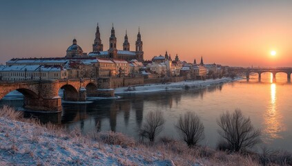 Fototapeta premium Cityscape at sunrise. A river flows beside buildings and bridges; snow-covered ground