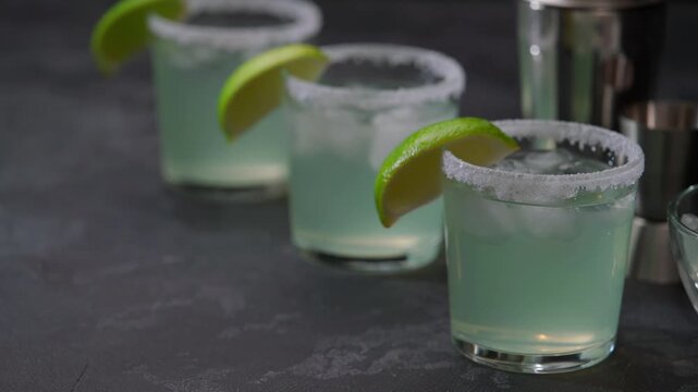 Many glasses of Margarita cocktail in a line. Three glasses in row with cocktail Margarita and fresh lime on a black table.
