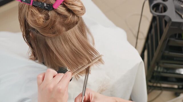 salon stylist crafting layered textured haircut rear view of client hair sectioned with clips, stylist combing and cutting fringe, fine hair dust falling, tools on trolley, energetic salon vibe,