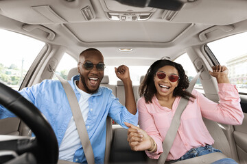 Yes, Summer Vacation Concept. Portrait of excited playful black couple in sunglasses driving car,...