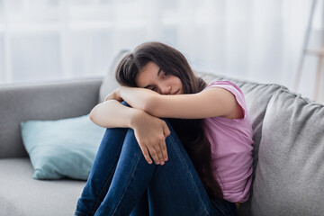 Unhappy teen girl feeling depressed or desperate, sitting on couch at home. Indian asdolescent...