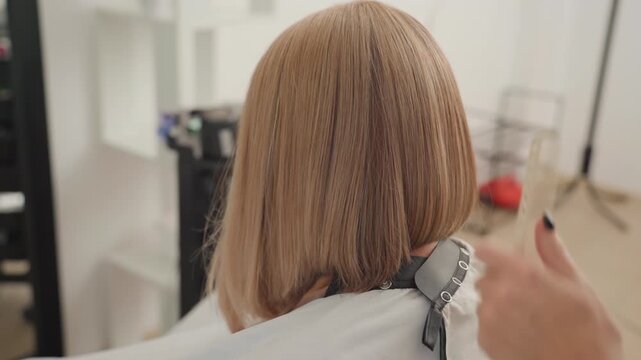 Back view white woman receiving bob trim with clipper and comb by focused stylist in minimalist salon, sleek shoulderlength blonde hair, precise straight edge, calm professional mood