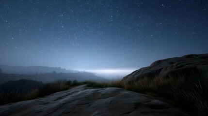 A vast starry night sky hovers over serene misty mountain ranges with a bright horizon glow and rugged rocky terrain in the foreground