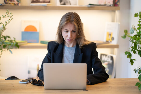 Relaxed businesswoman freelancer using laptop at cafe, working on remote in cozy workplace, typing or doing research online on computer. Female enjoying remote office work lifestyle in casual setting. - Powered by Adobe