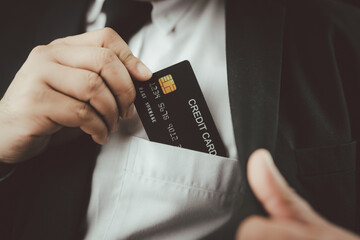 Cropped view of male executive of a wearing dark suit and white shirt taking a black credit card out of his front pocket