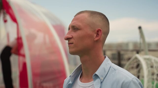Rooftop man gazing over urban skyline, thoughtful portrait capturing evening light, wind ruffling crewcut hair, casual shirt and subtle expression, rooftop railing and distant buildings framing scene,