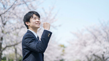 満開の桜を背景に拳を握って喜ぶ日本人男子高生