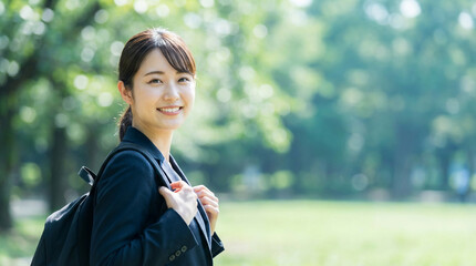 新緑の公園でスーツ姿で微笑む日本人女子大学生
