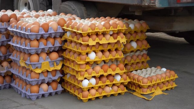 A large quantity of eggs, both brown and white, are stacked in yellow and purple cardboard containers next to a truck. A few containers are partially empty