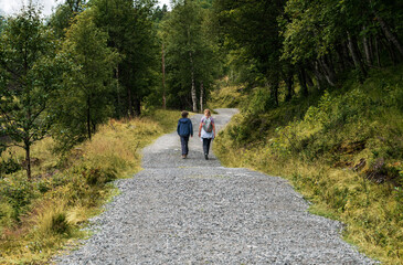 Obraz premium A mother and her son walk along a gravel path in Innerdalen Valley, Norway. They enjoy hiking and spending quality time together in nature surrounded by trees and hills. 