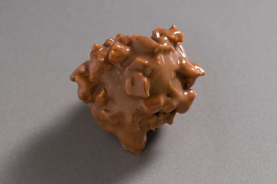handmade milk chocolate rocher with crunchy almond pieces on grey background