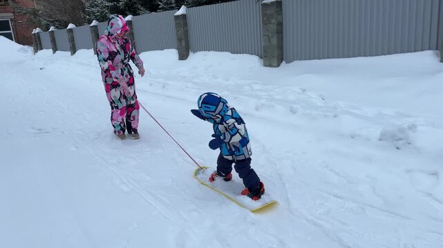 A mother teaches a little boy to snowboard.