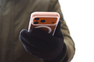 Close up of a gloved hand holding a modern smartphone isolated on a white background. Concept of mobile technology, privacy, security, cold weather usage, and digital communication.