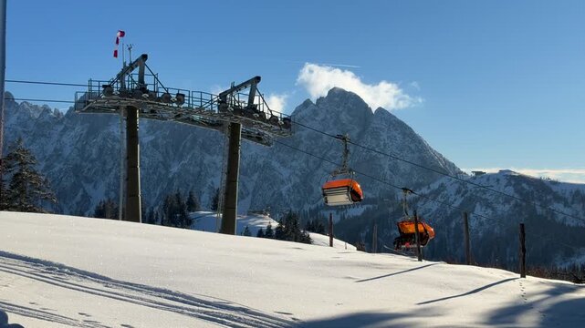 Modern ski lift chairs moving uphill on a sunny winter day in Austria with the Alps in the background. Snow covered slopes and blue sky create a bright alpine mountain scene