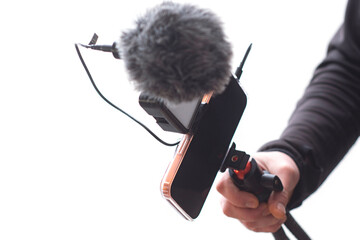 Smartphone in hand mounted on a handheld vlogging rig with LED light and external microphone....
