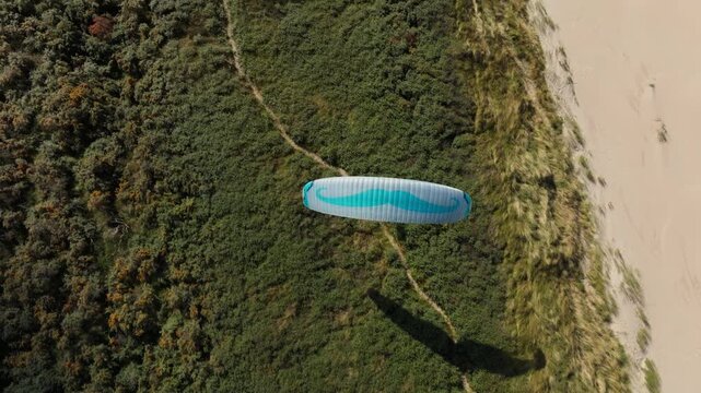 Top view over paraglider soaring along vegetated Dutch coastal dune