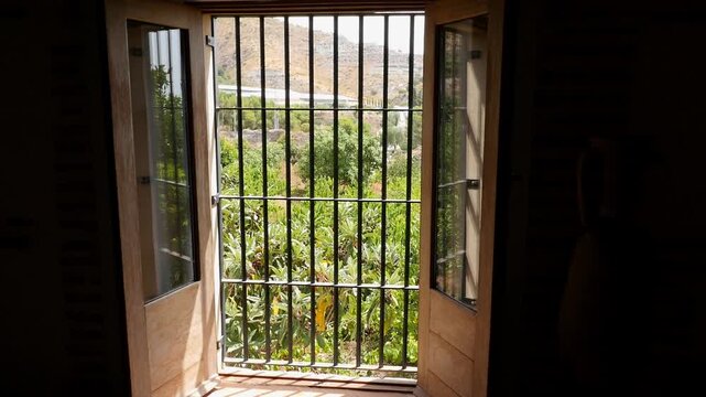 View from a window with wrought iron grilles. A dense plantation of loquats and the sunny agricultural landscape of Granada can be seen.