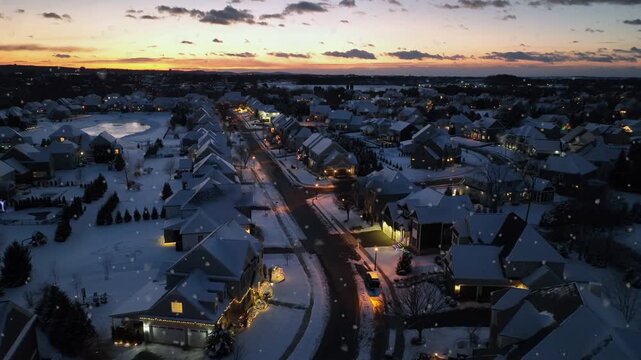 Soft snowfall in upper class residential area with snow-covered houses in america. Aerial establishing shot. Peaceful suburb neighborhood at golden sunset on cold winter day. Wide shot.
