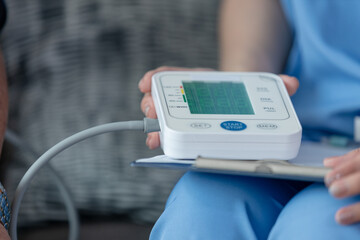 Close-up of digital blood pressure monitor held by nurse during home health check, highlighting remote healthcare, elderly care and accurate medical diagnostics.