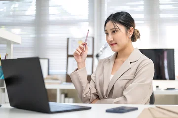 Fotobehang Diamanten Pretty asian businesswoman or office worker holding pencil thinking while looking at laptop on table  © bongkarn
