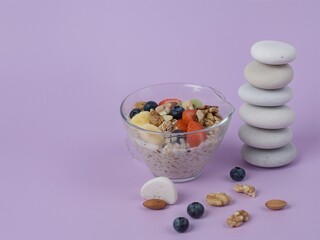 Breakfast bowl with fruit and nuts, stack of stones on purple background