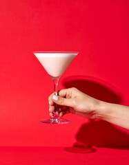 Elegant Hand Holding Sweet Pink Martini Cocktail Against a Bold Red Background in Studio Lighting
