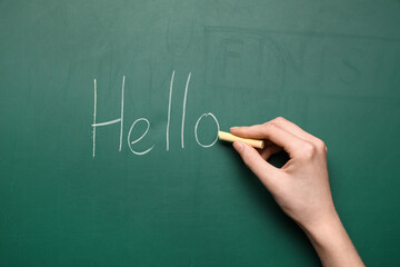 Woman writing text Hello with yellow chalk on green blackboard © Pixel-Shot