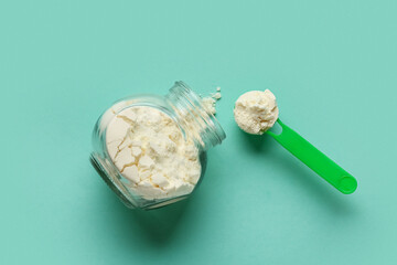 Jar of powdered milk with measuring scoop on turquoise background