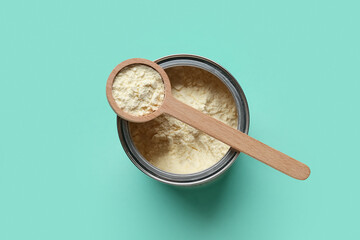 Container of powdered milk with wooden measuring scoop on turquoise background