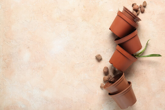 Plastic flower pots with clay pebbles and plant leaves on beige grunge background