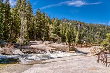 A beautiful mountain landscape with a river flowing through it. The water is rushing and the trees are lush and green. The sky is clear and blue, creating a peaceful and serene atmosphere