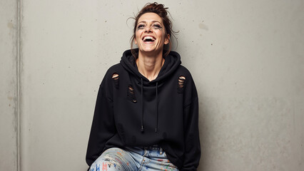 Confident woman laughing wildly in oversized torn hoodie against concrete wall  