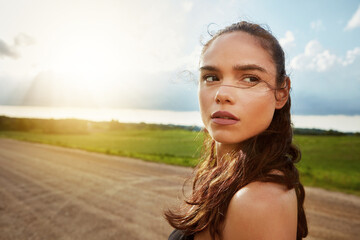 Blue sky, exercise and running with woman in countryside for commitment to cardio training outdoor. Clouds, fitness or space with thoughtful runner on dirt road in nature for challenge or improvement