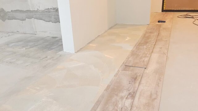 Workers prepare the floor for new laminate and quartz vinyl installation in a building. The surface is leveled and drying occurs before any further steps are taken.