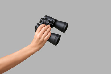 Female hand holding modern binoculars on grey background