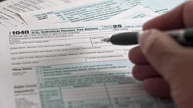 A person is filling out a 140 U.S. individual income tax form. The setting is likely a home or office. Papers are organized on a surface with a pen in hand, showing diligence.