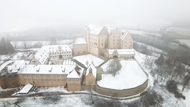 Drone moves backward revealing full architectural complexity of Schloss Kapfenburg with gabled towers, multiple courtyards, chapel, and surrounding walls snow-blanketed on the Ostalb. Complete fortres