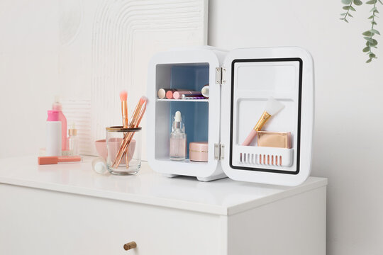 Small refrigerator with cosmetic products on chest of drawers near white wall