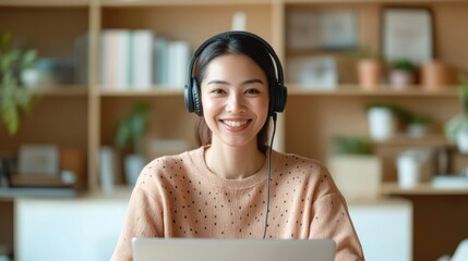A young woman wearing headphones smiles while working on a laptop in a cozy, modern workspace filled with plants.